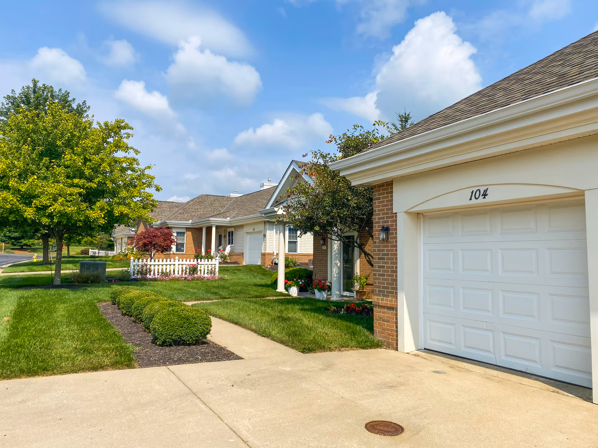 Exterior view of Knolls of Oxford, single-story townhomes with garages and green landscaping.
