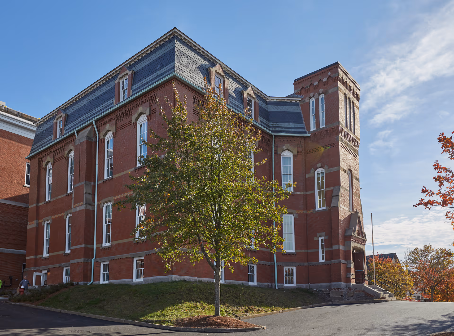 Red brick senior living building with a tree in the foreground and blue sky.