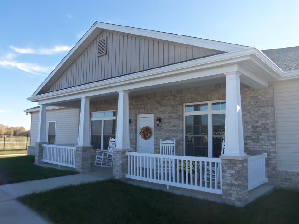 Front porch of a brick senior living facility with rocking chairs and a wreath