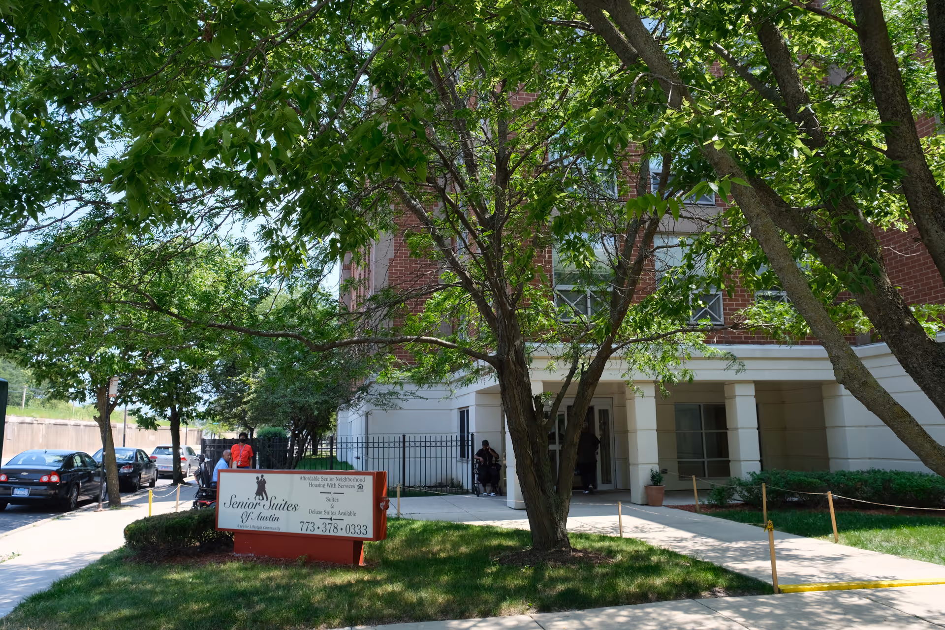 Front entrance of the Senior Suites of Austin building with a lawn sign, trees, and a sidewalk.