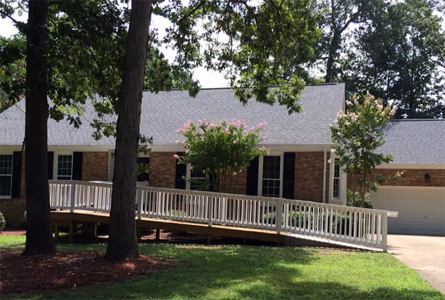 Front view of Avendelle Assisted Living building with ramp, trees, and brick facade.