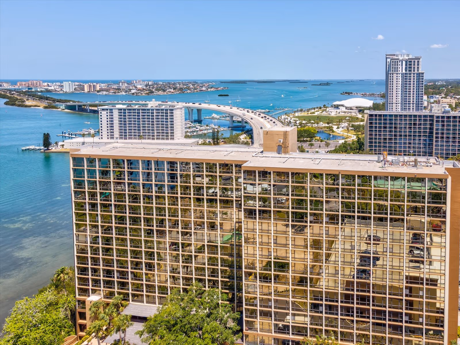 Tall glass-fronted senior living building by the water with a distant bridge and ocean view.