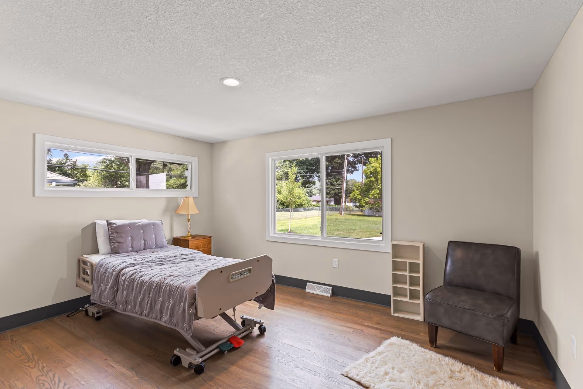 A furnished bedroom with an adjustable bed, nightstand, lamp, and large window view.