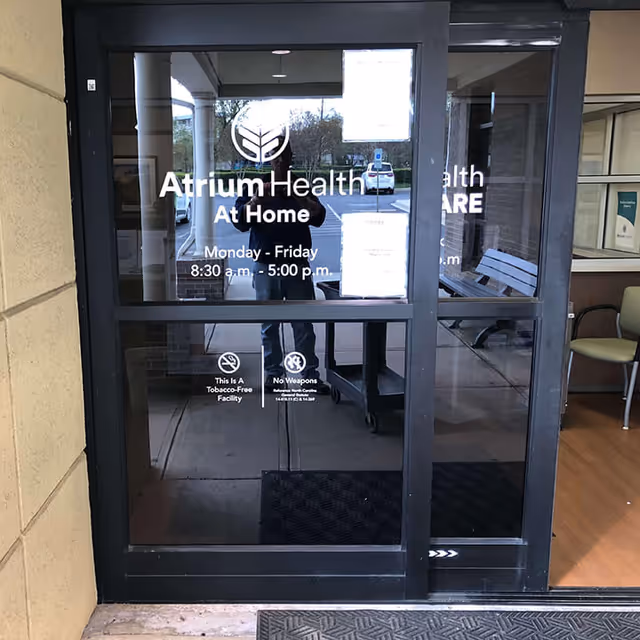 Glass entrance door with Atrium Health At Home HME Union signage and photographer's reflection.