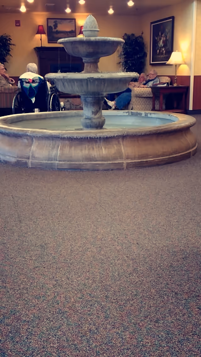 Indoor lobby with a central fountain, seating, and seniors seated around.