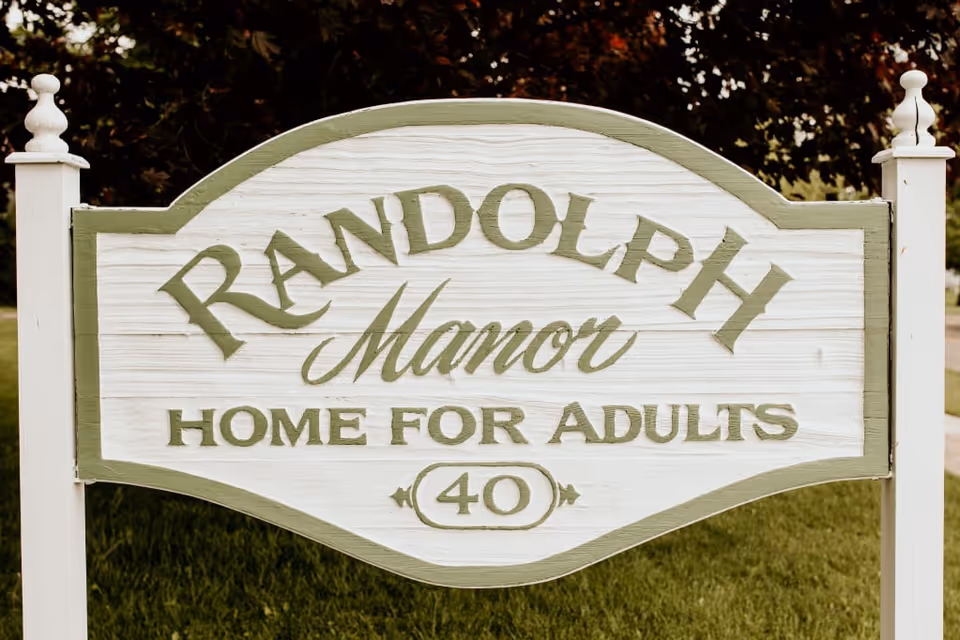 Large wooden Randolph Manor sign on a grassy lawn reading Home for Adults 40.
