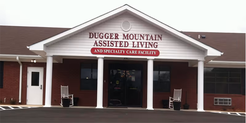 Front view of Dugger Mountain Assisted Living facility with pillars, rocking chairs, and a parking lot.
