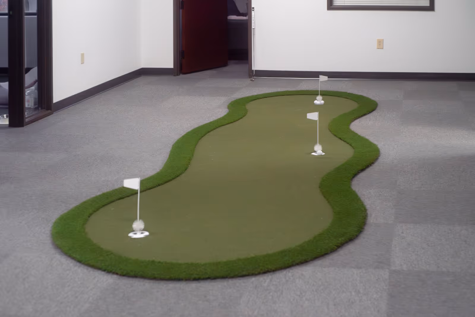 Indoor senior living facility hallway with a small artificial putting green on gray carpet