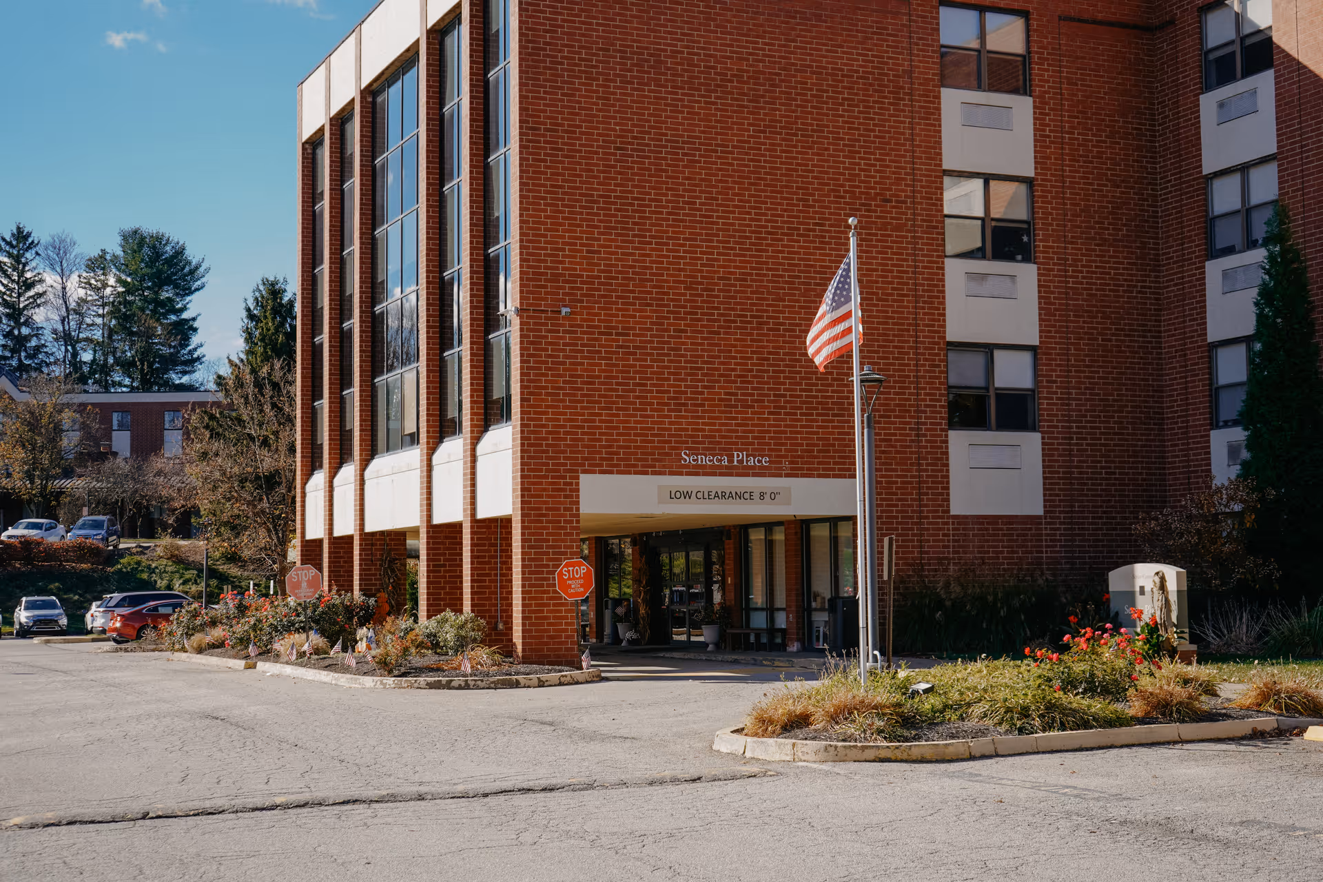 Front entrance of a brick building labeled 'Seneca Place' with an American flag, driveway, and landscaping.