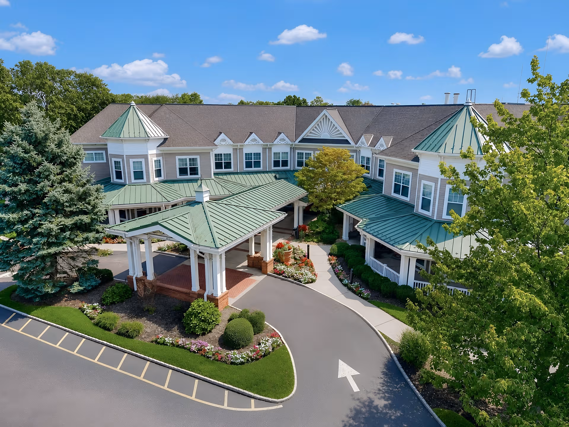 Aerial view of Sunrise of Woodcliff Lake exterior with green metal roofs and entrance.