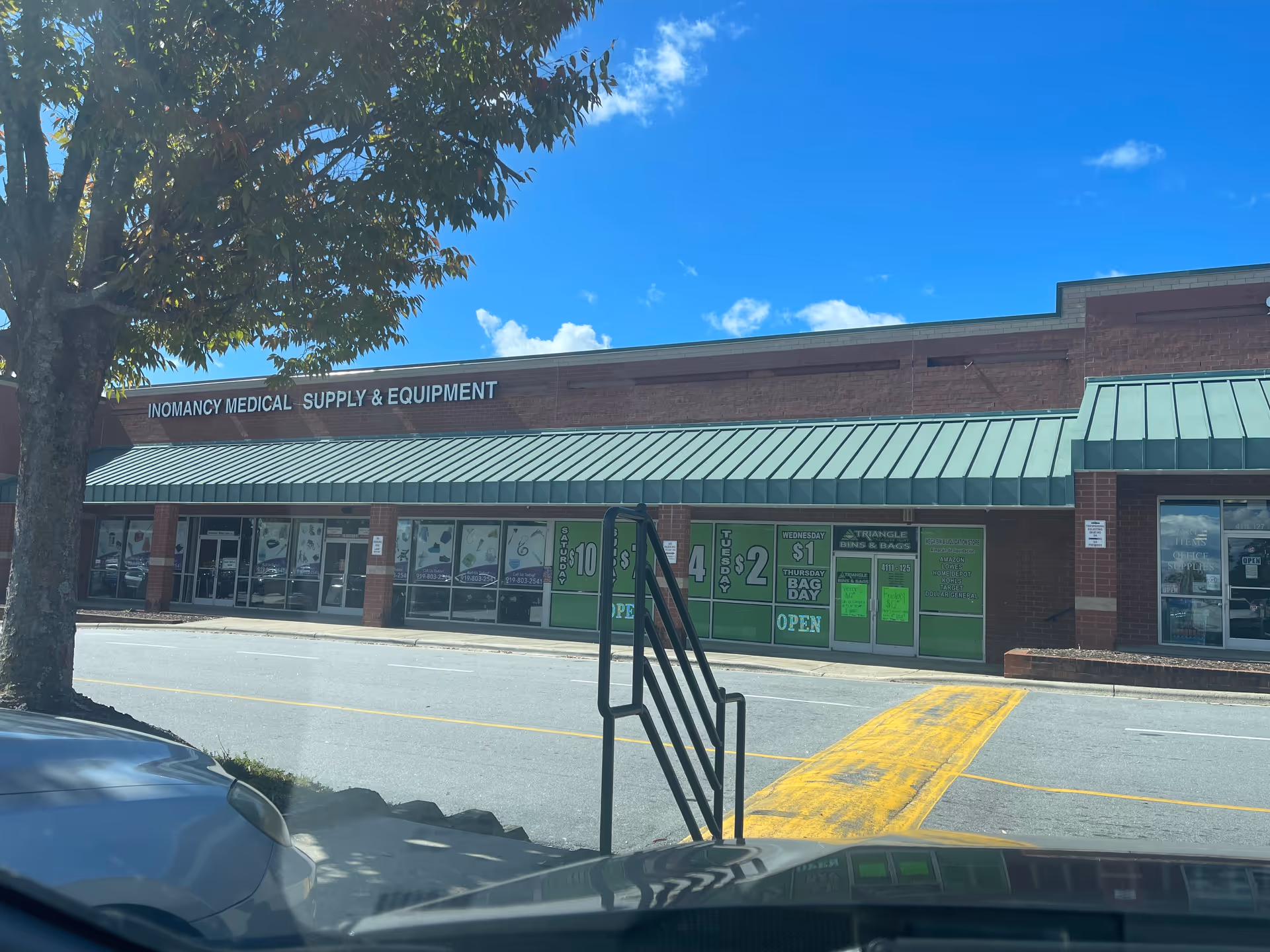 Exterior view of a strip mall storefront reading Inomancy Medical Supply & Equipment against blue sky