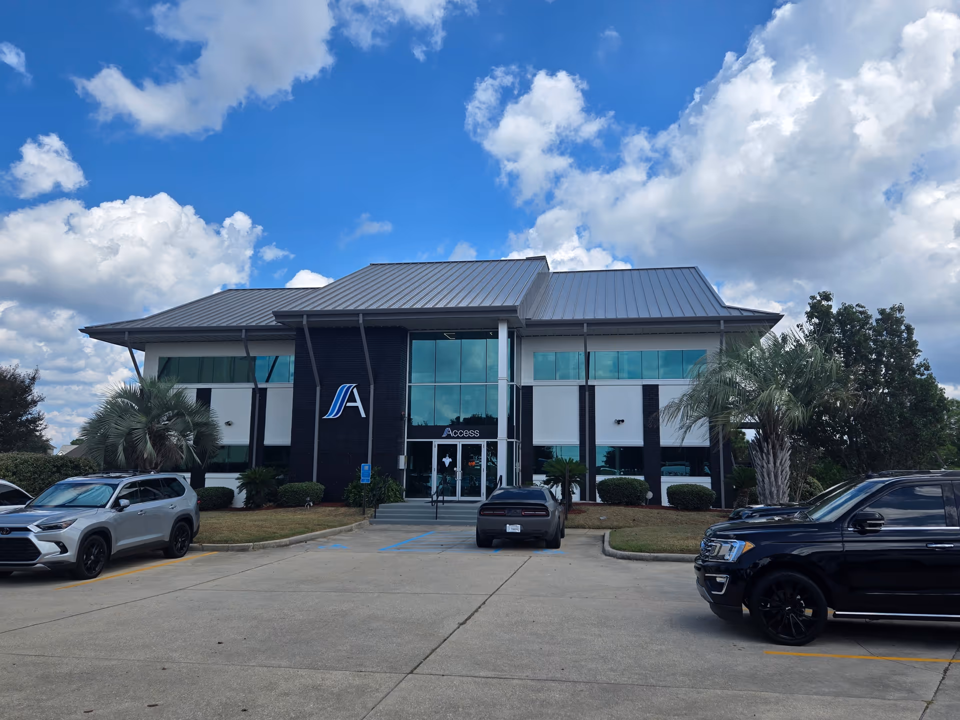 Modern two-story facility with glass entrance and several parked cars.