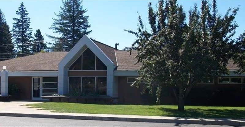 Single-story building with a triangular front entrance, large windows, and a tree in the front yard.