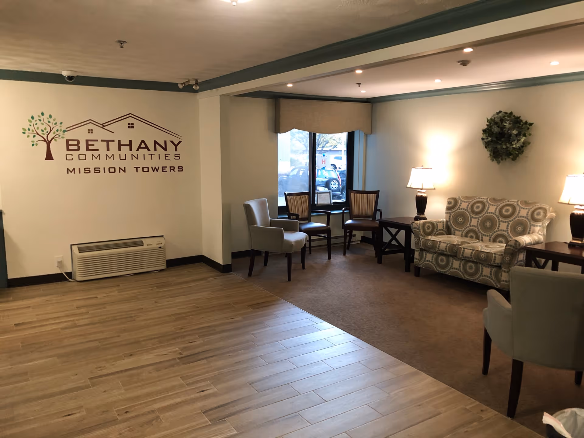 Lobby lounge at Mission Towers with seating, tables, lamps, and a wall logo.