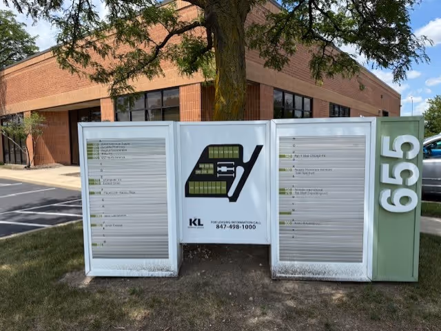 Exterior brick building with a three-panel outdoor directory sign and a tree.