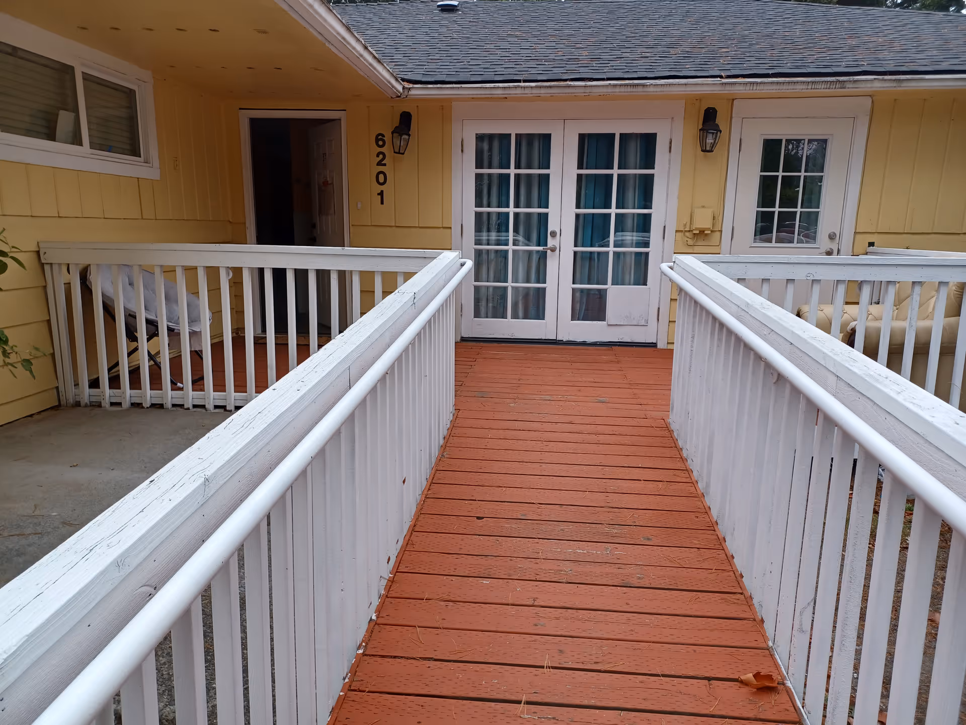 Yellow facility exterior with a wooden ramp and white railings to glass double doors.