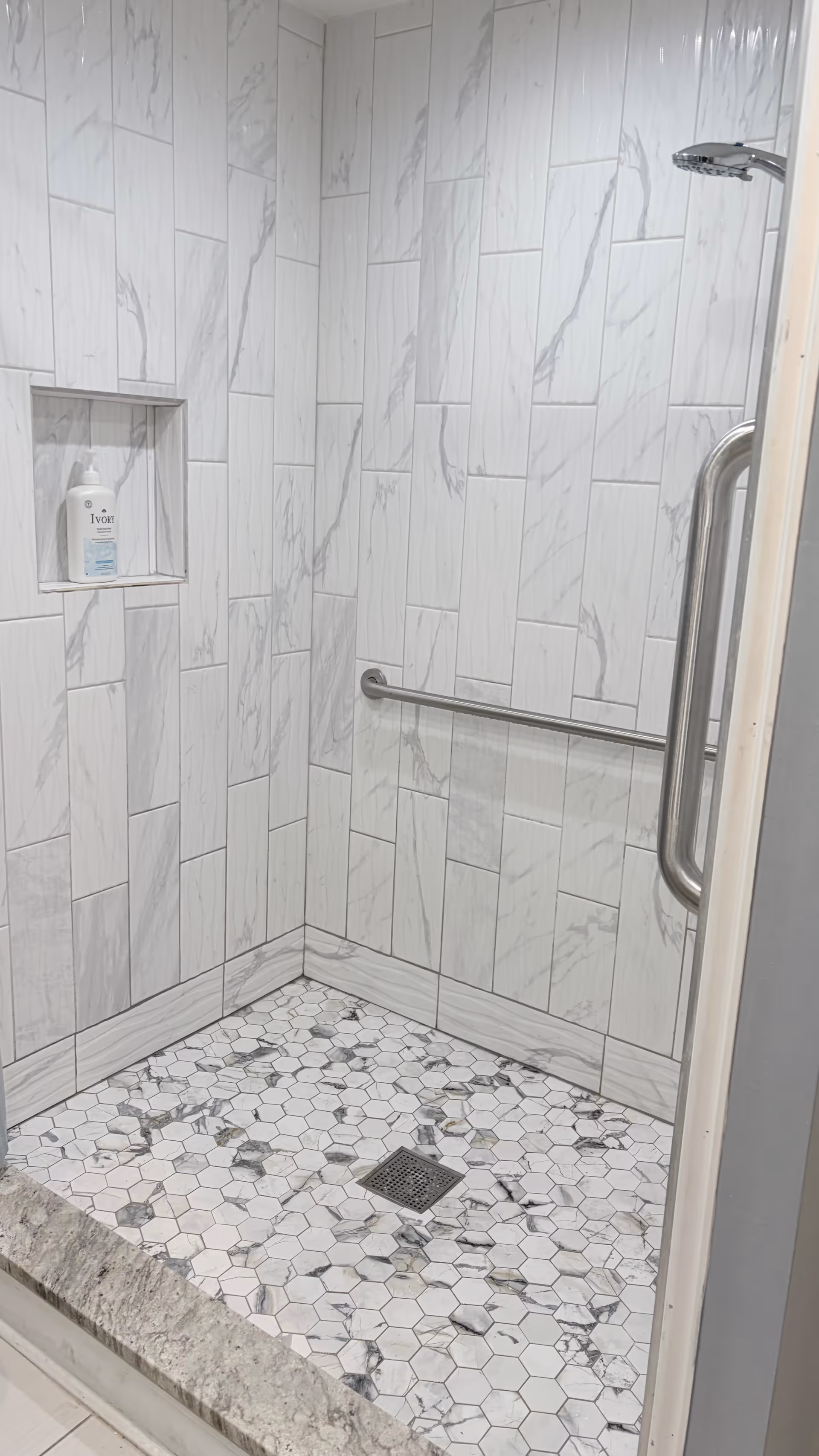 Shower stall with marble-look tile walls, soap niche, grab bar, and hex mosaic floor.