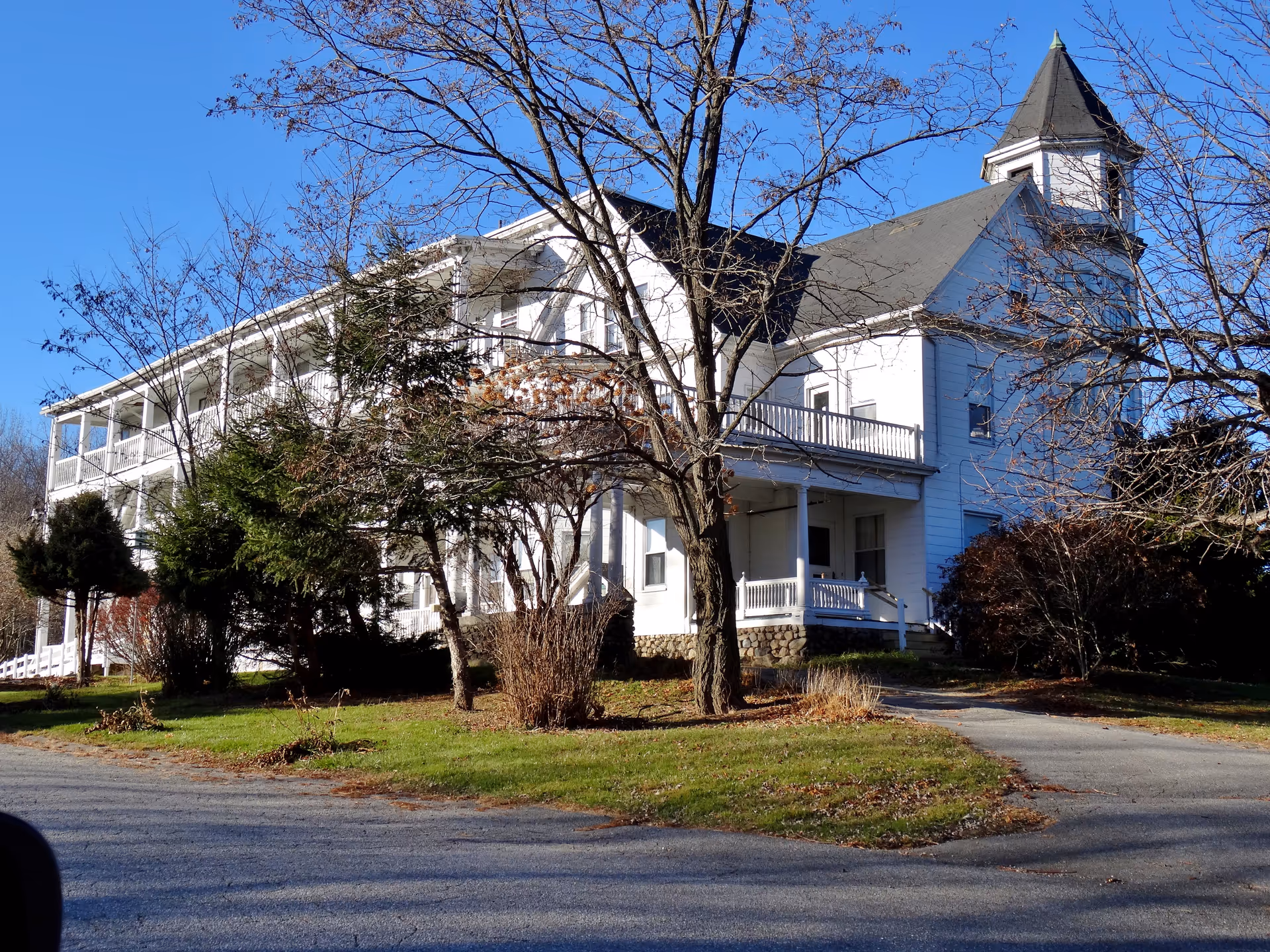 A white residential care building with a wraparound porch and leafless trees.