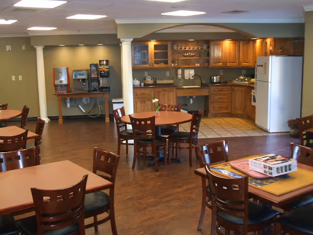 Senior living dining area with round tables, chairs, and a kitchen in the background.