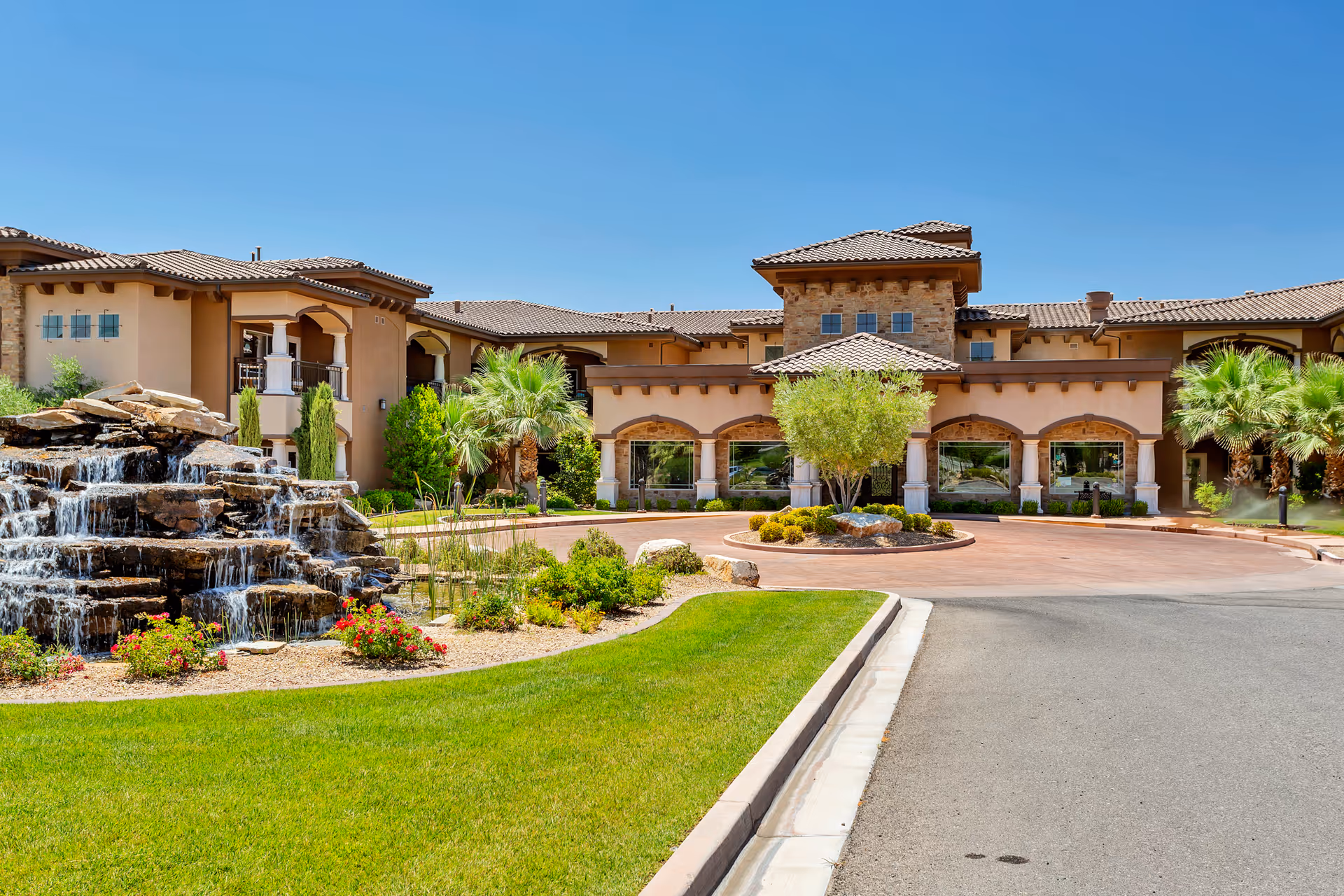 Front exterior of The Retreat at Sunbrook, featuring a waterfall, palm trees, and a circular driveway.