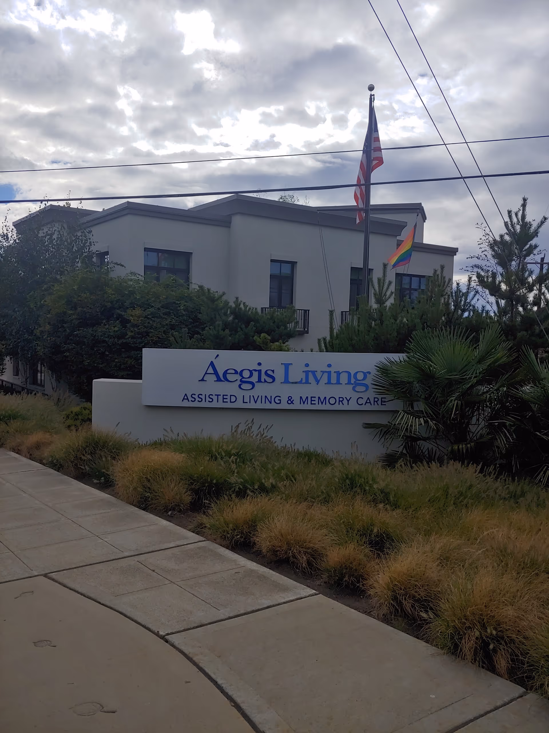Front exterior of Aegis Living West Seattle with sign, flags, and landscaping.
