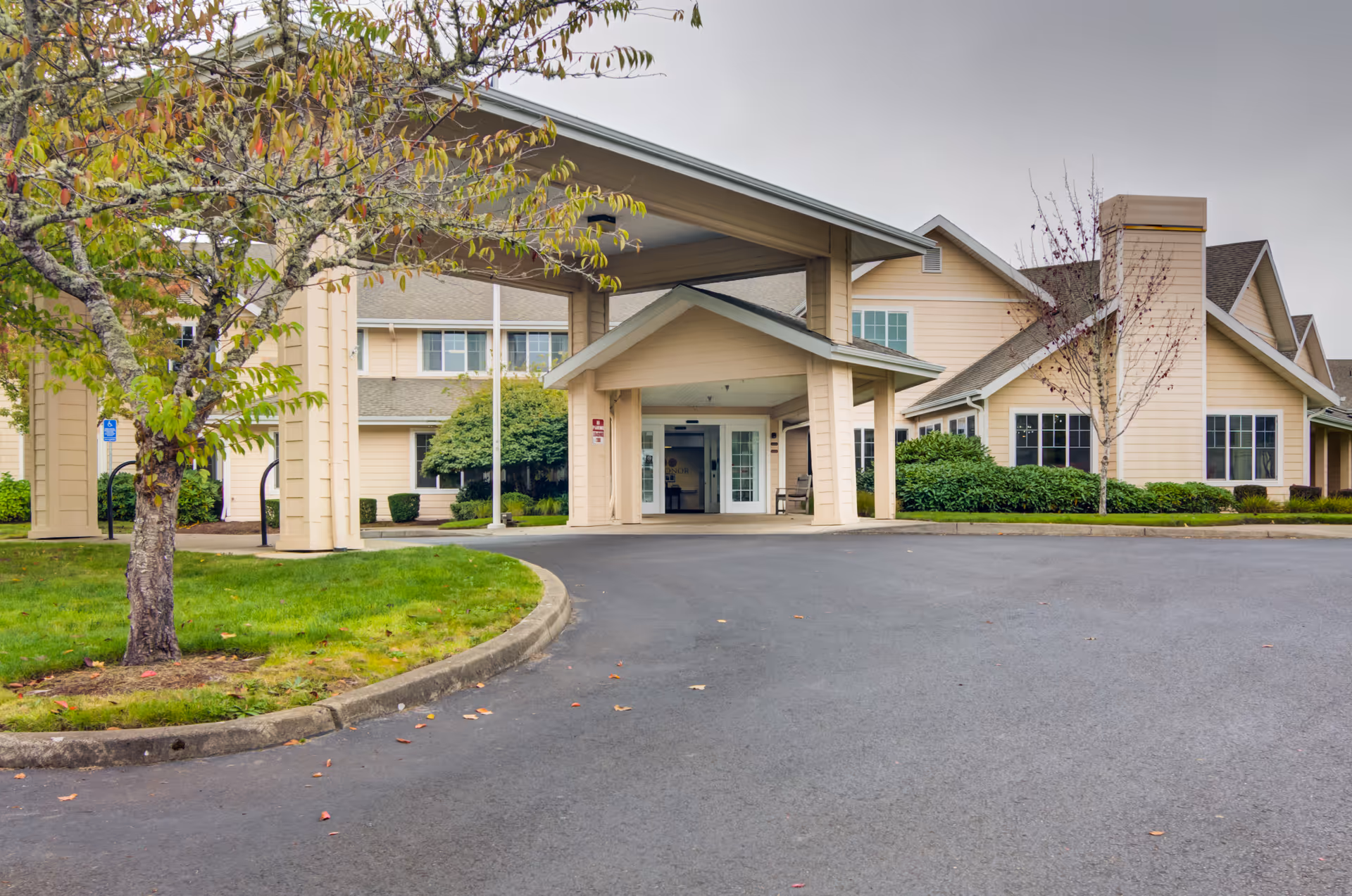 Exterior view of a beige senior living facility with a covered entrance and parking.