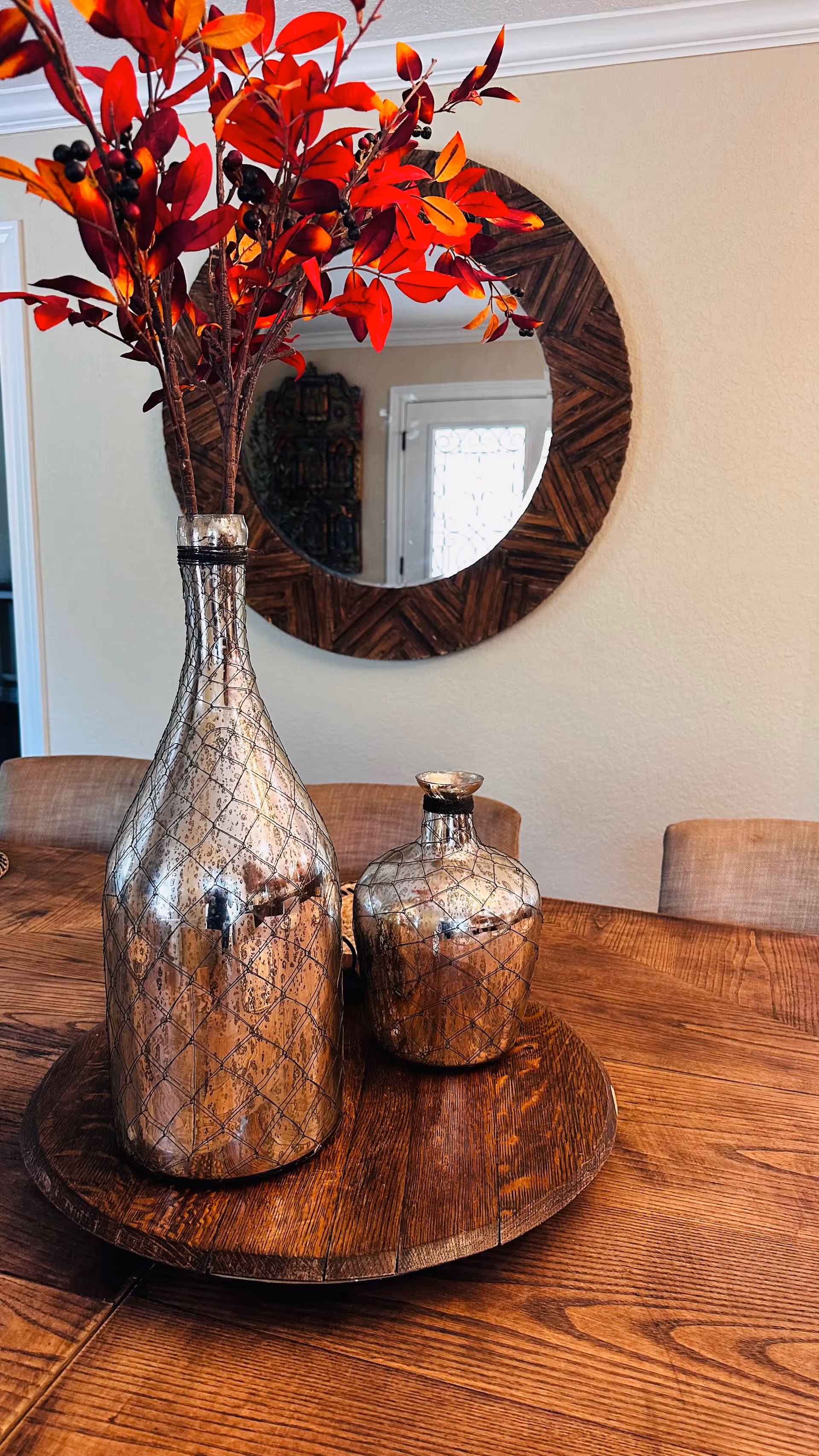 Decorative vases sit on a wooden dining table with a round mirror on the wall.