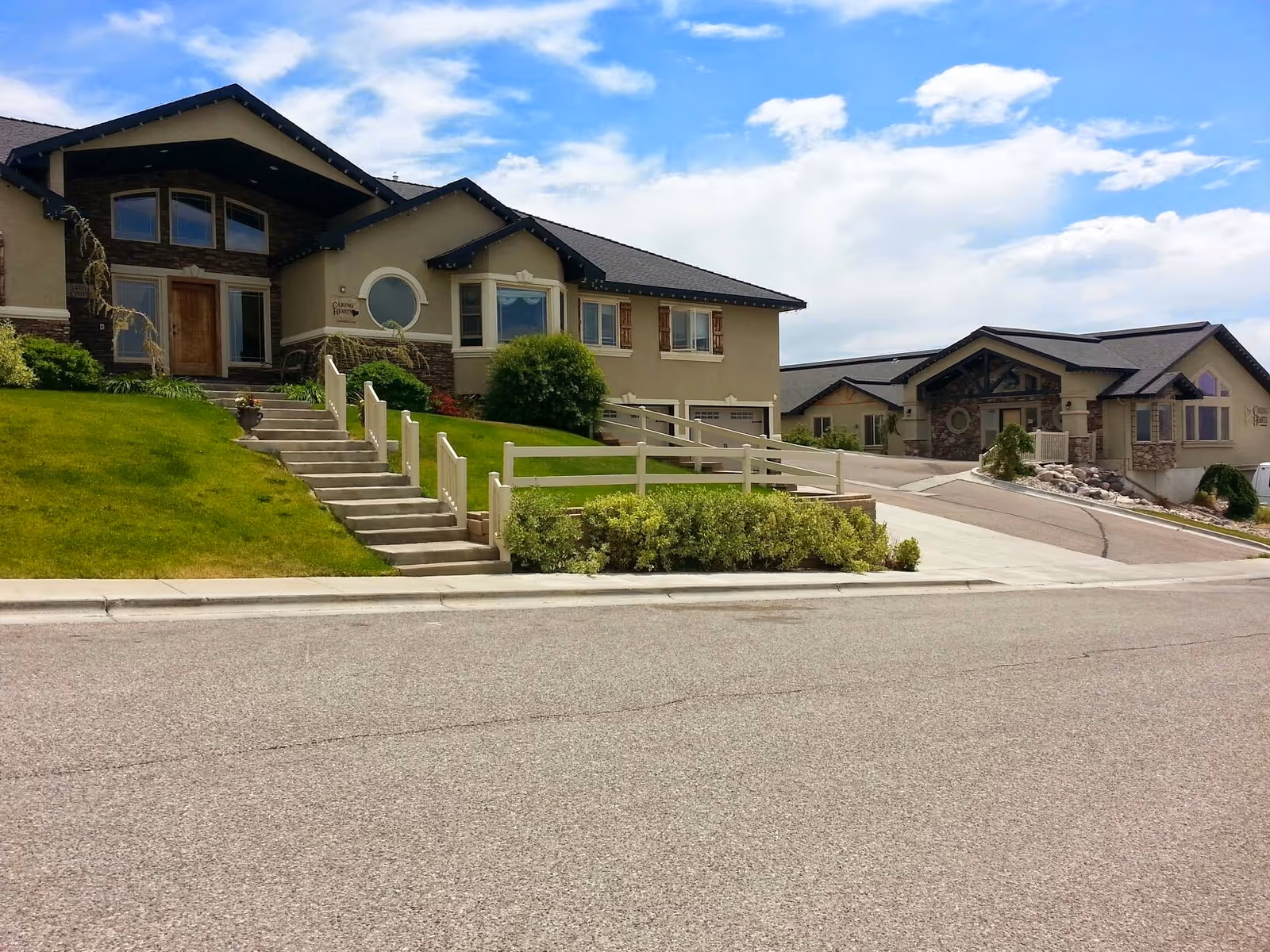 Exterior view of Caring Hearts Assisted Living with multiple connected buildings, steps, and a green lawn.
