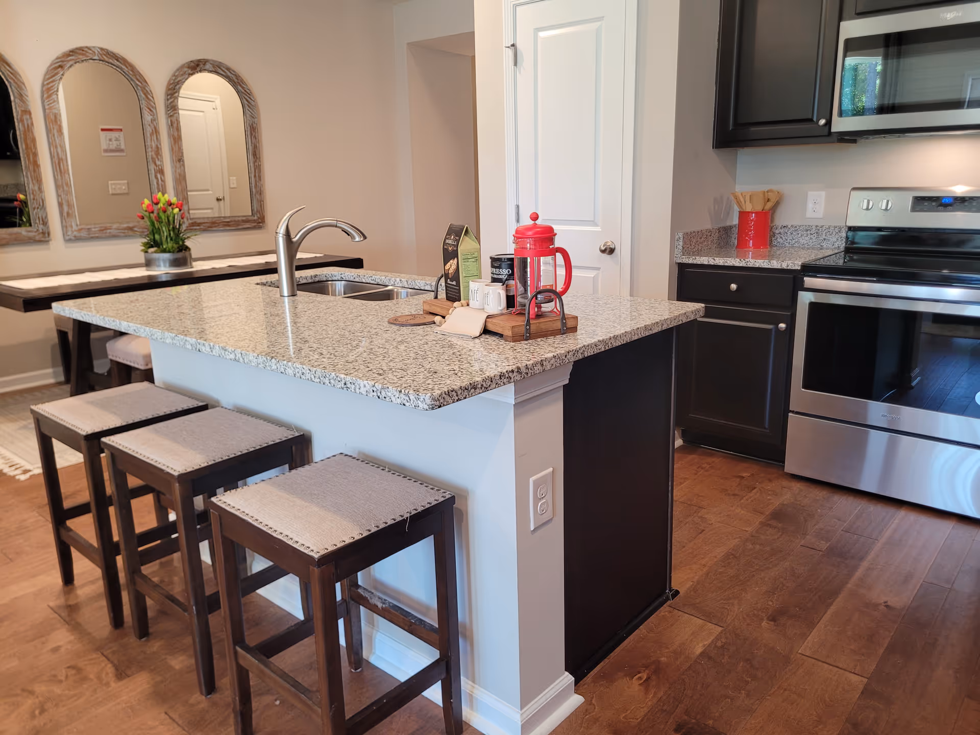 Modern kitchen with island, stools, granite countertop, black cabinetry, and stainless appliances.