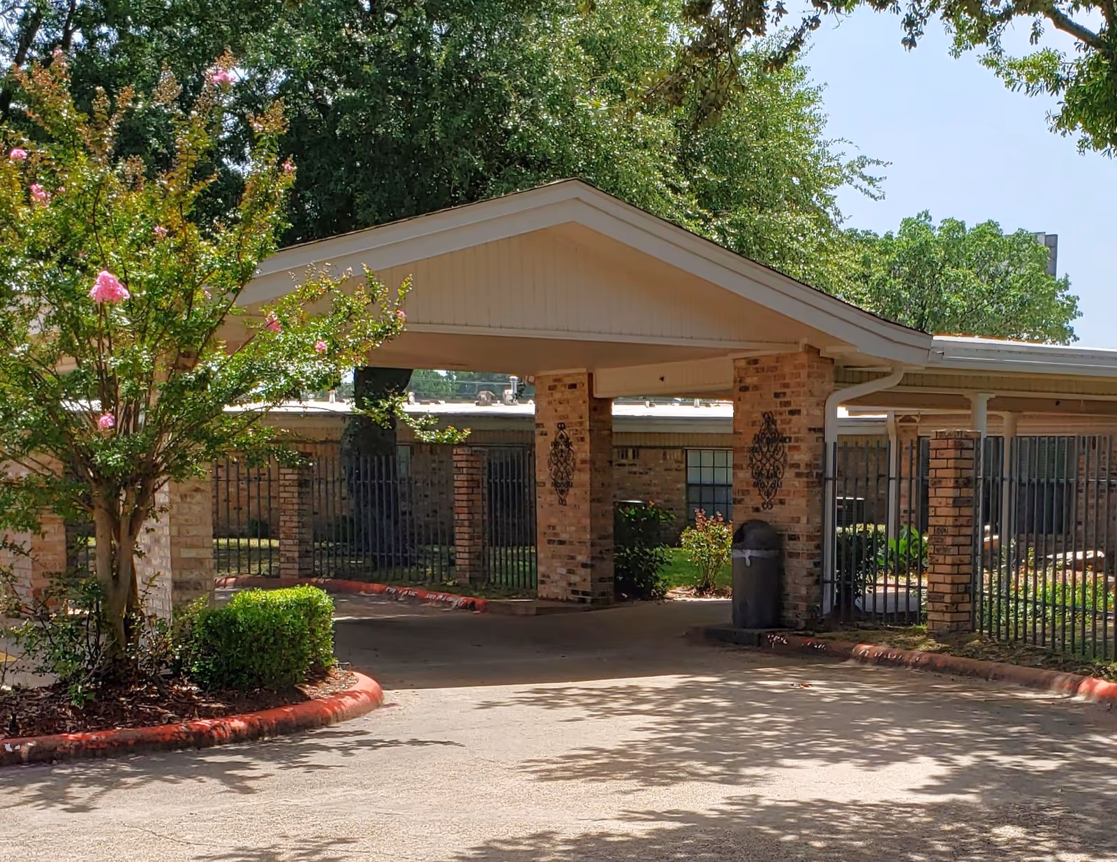Entrance to Pleasant Springs Healthcare Center with a covered driveway, brick columns, and greenery.