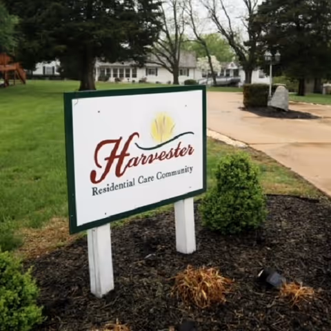 An outdoor sign for Harvester Residential Care Community sits in front of a grassy lawn