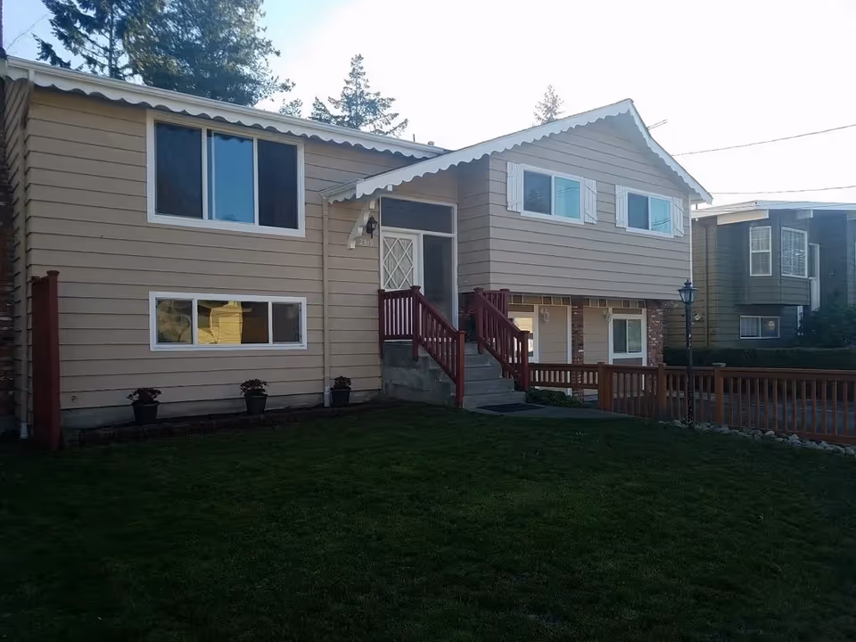 Two-story beige house with white trim, red stair railings, and a green front lawn.