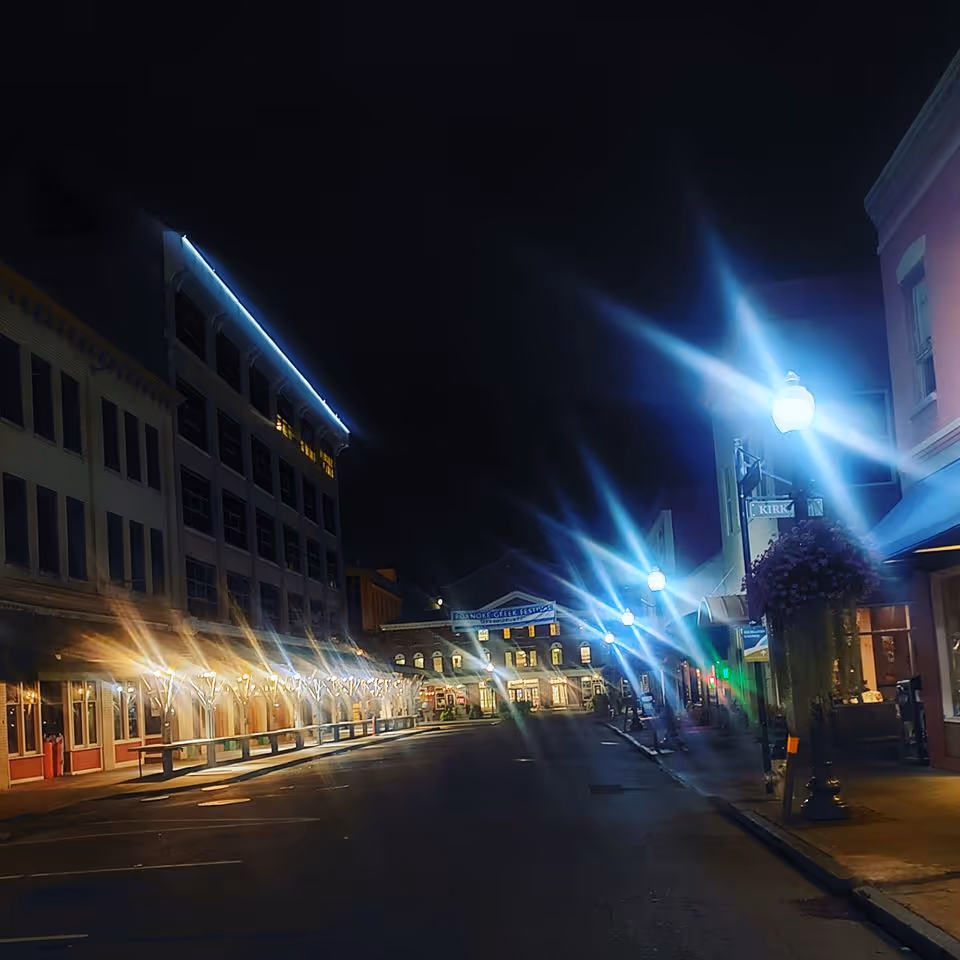 Nighttime street scene with illuminated storefronts and blue streetlights along a quiet downtown.