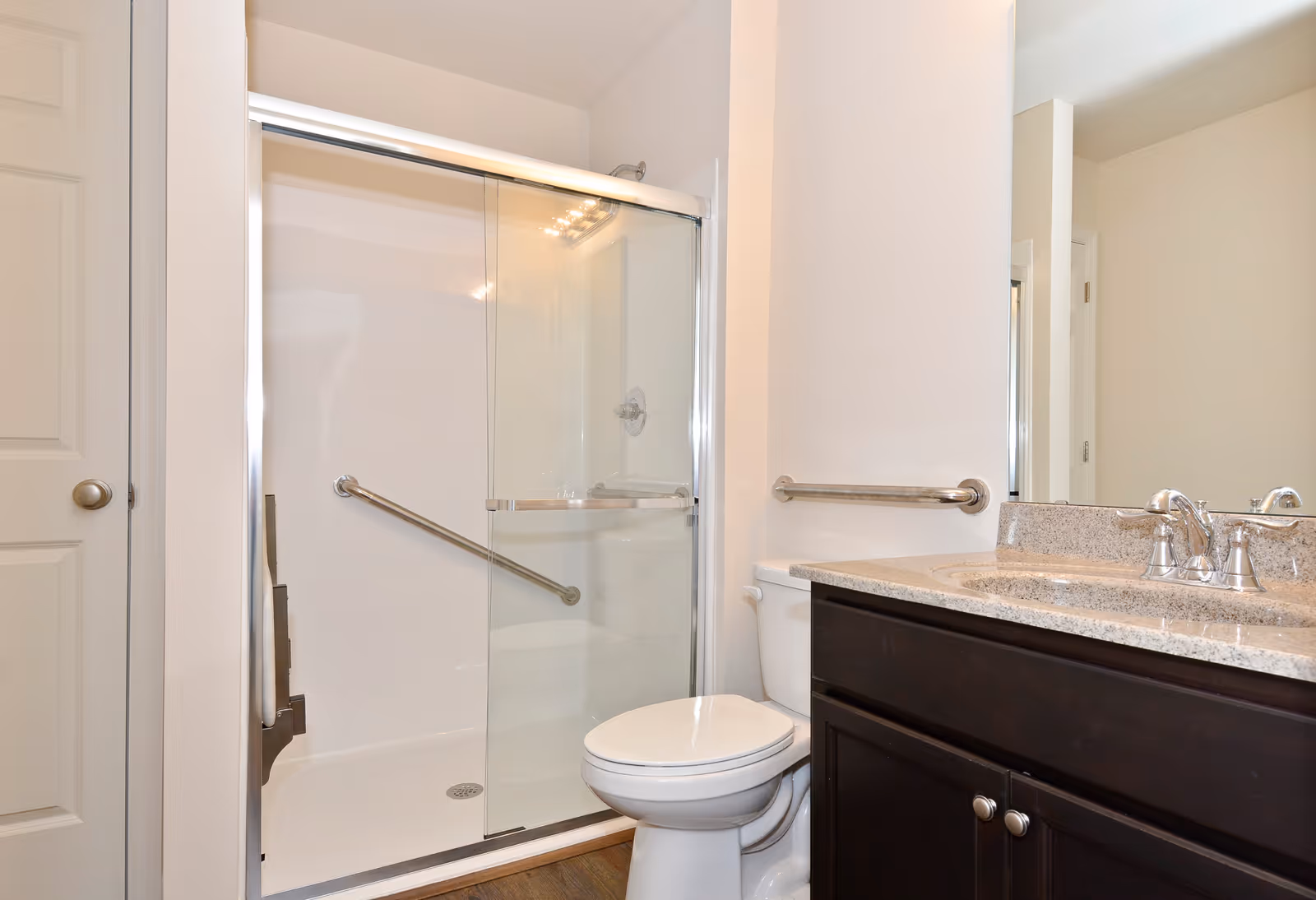 Modern bathroom in a senior living facility with a glass shower and dark vanity.