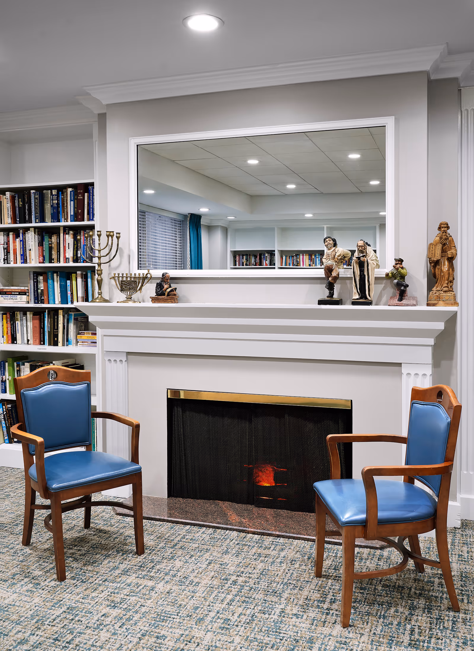 Cozy living room with a fireplace, two blue chairs, and bookshelves.