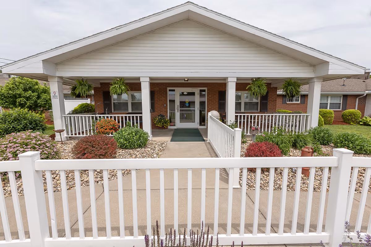 Front entrance of a senior living facility with a white railing and landscaped garden.