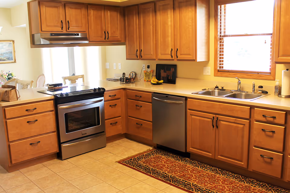 Bright kitchen with wooden cabinets, stainless steel stove and dishwasher, double sink, and a patterned rug.