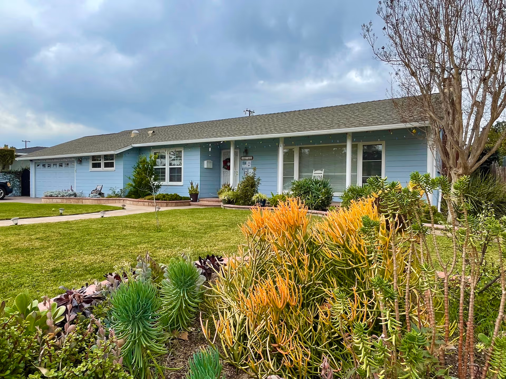 Single-story blue senior care facility with a manicured lawn and shrubs in front.