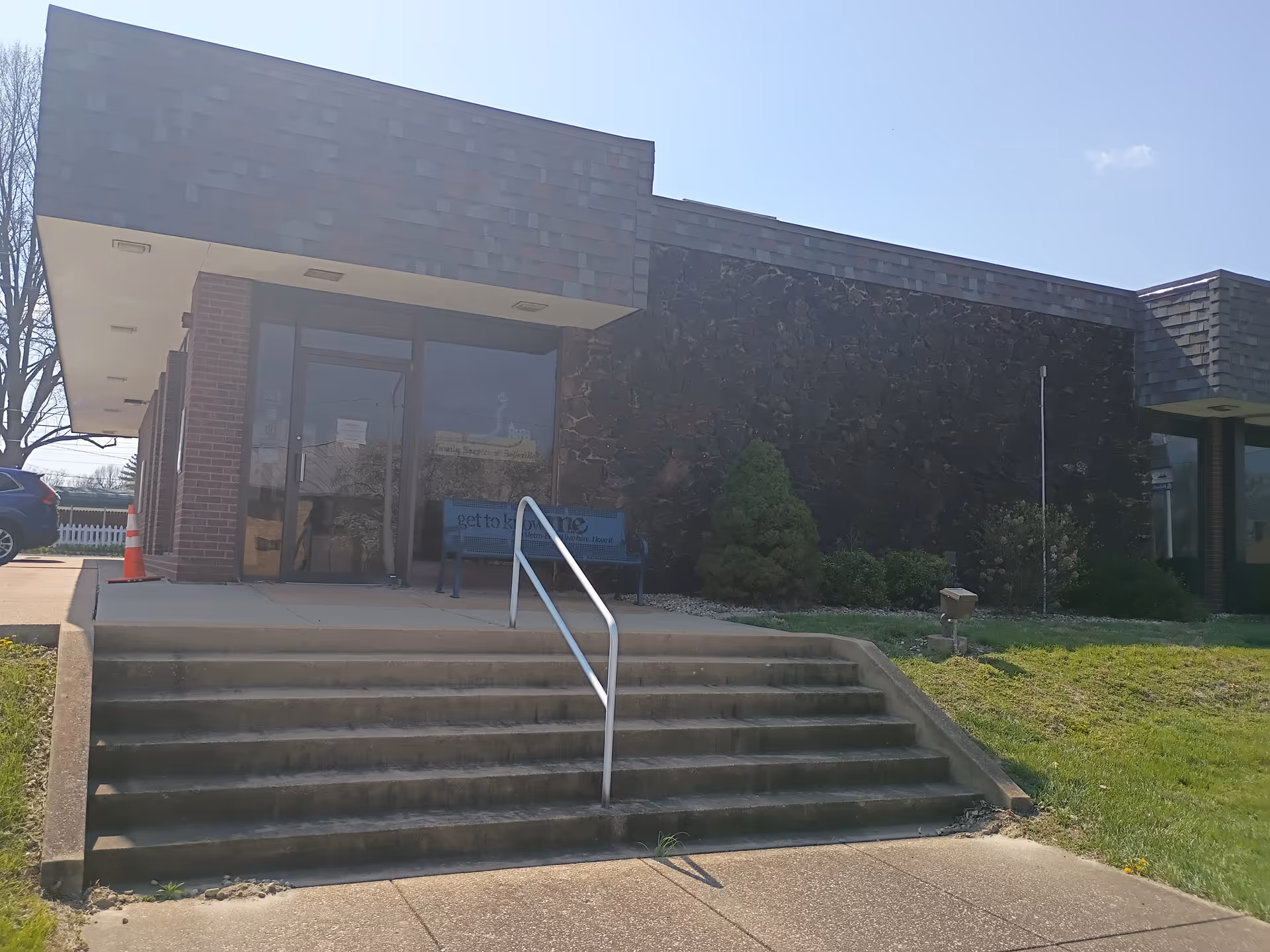 Exterior view of a senior living facility entrance with steps and glass doors.