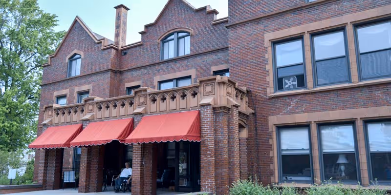 Brick front facade of Hume Home of Muskegon with red entrance awnings and a person seated near the doorway.