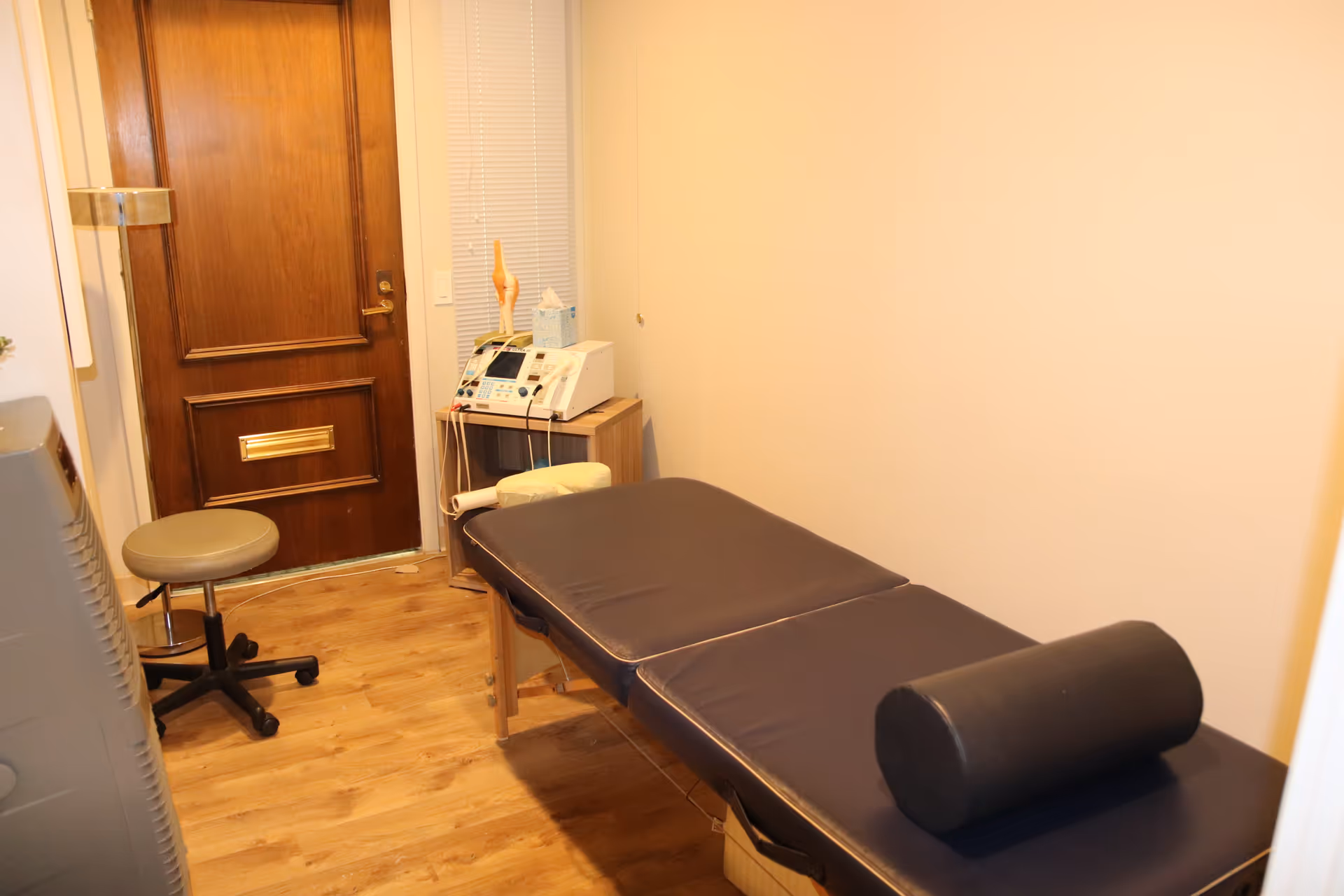 Small therapy room with an examination table, stool, and medical equipment.