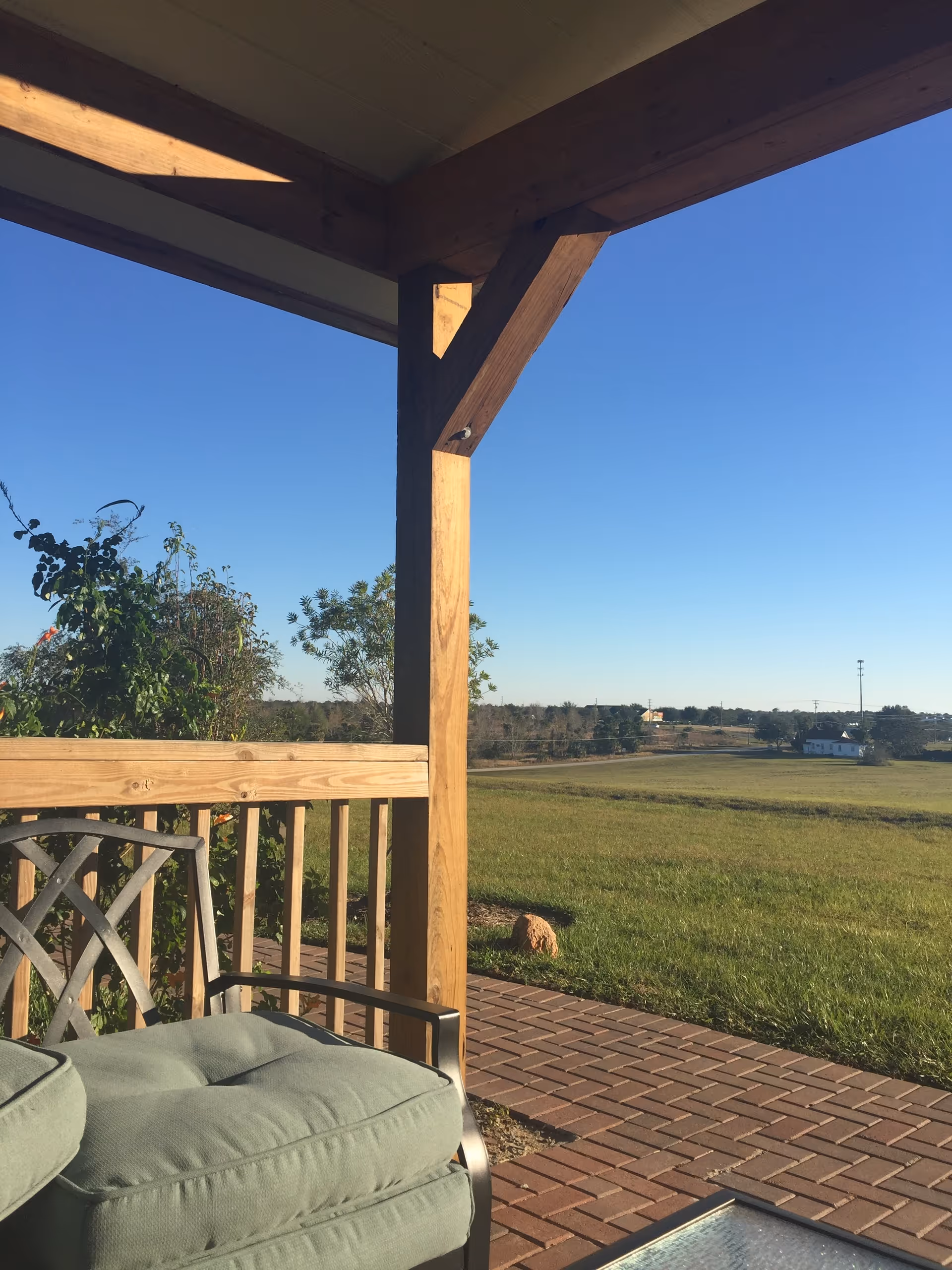 Outdoor porch with cushioned seating overlooking a grassy field on a sunny day.