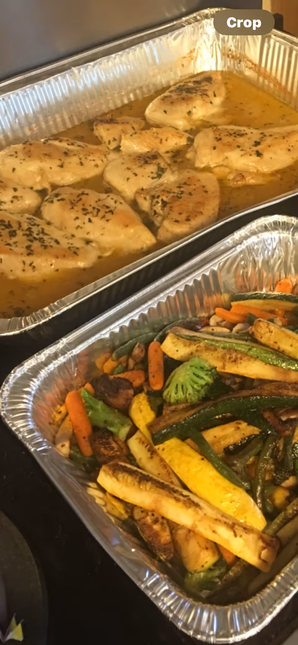 Aluminum trays hold seasoned chicken in sauce and roasted mixed vegetables.