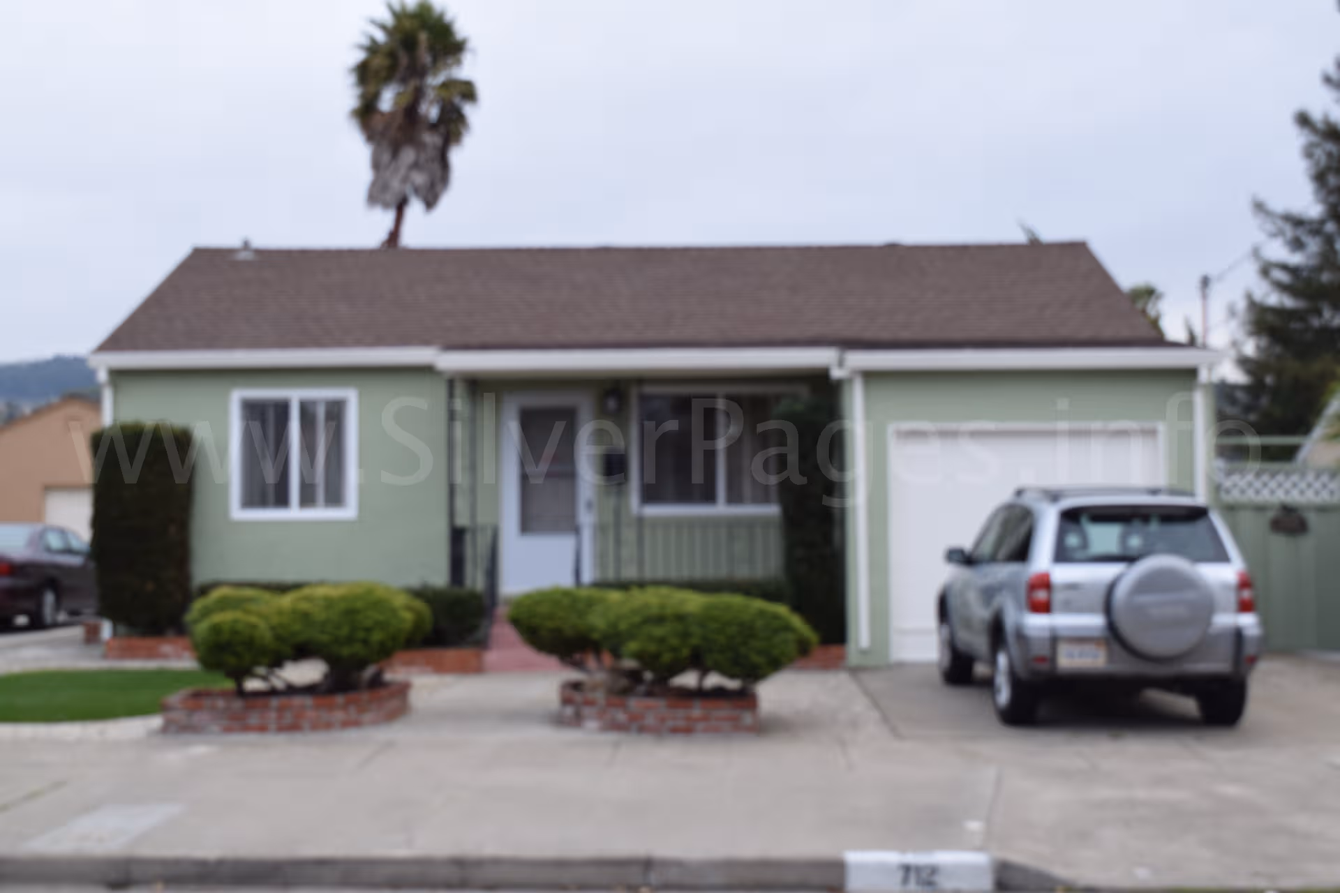 Front view of a green single-story building with a driveway and SUV.