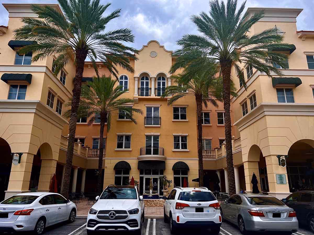 Sunlit peach-colored Bueno Care senior living building with arches, palm trees, and parked cars.