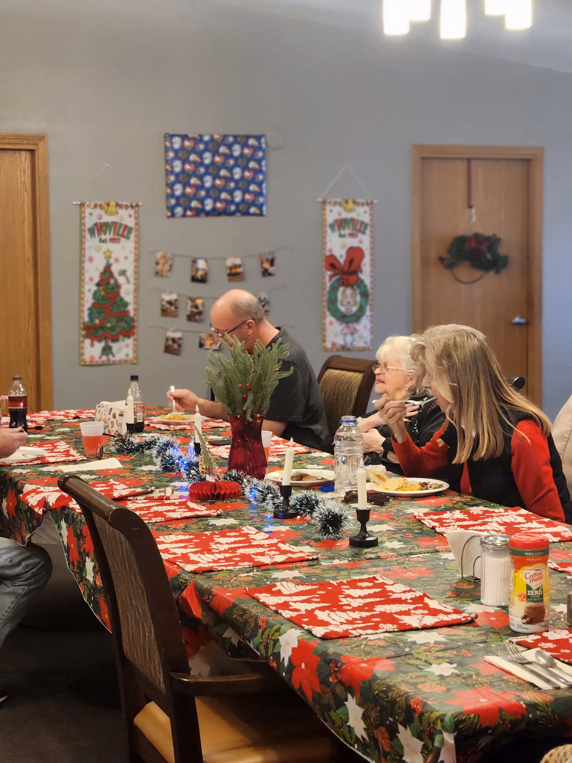 Residents sit at a long, holiday-themed dining table in a decorated senior living dining room.
