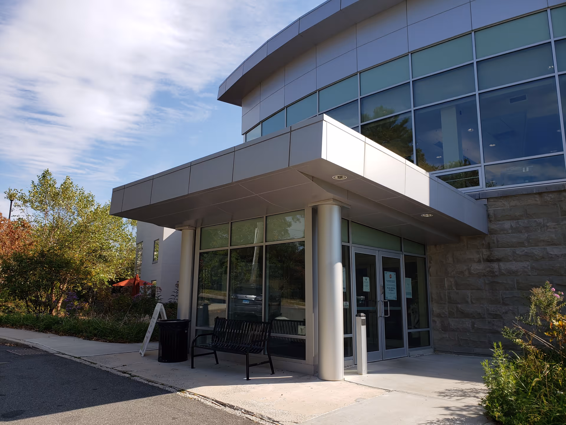 Wartburg Home exterior entrance featuring glass facade, curved canopy, large windows, and a bench.