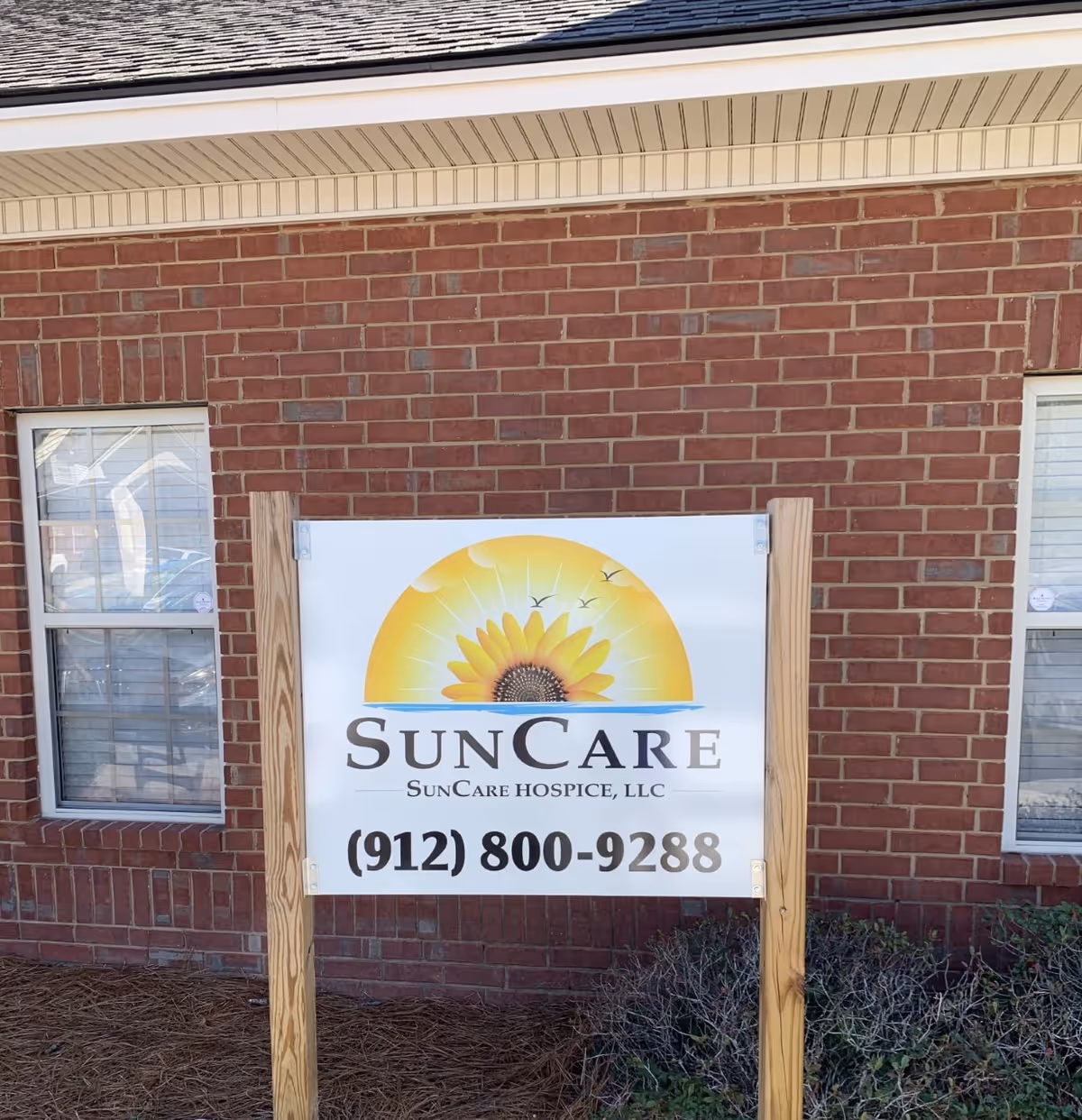 Sign with sunflower logo for SunCare Hospice on brick building exterior.