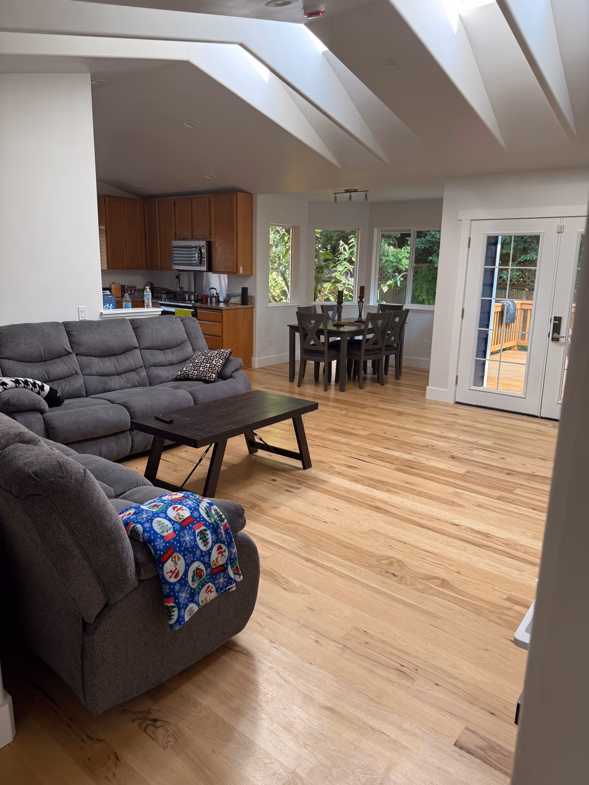 Open-concept living area with gray sectional, dining table, kitchen cabinets, and glass doors.