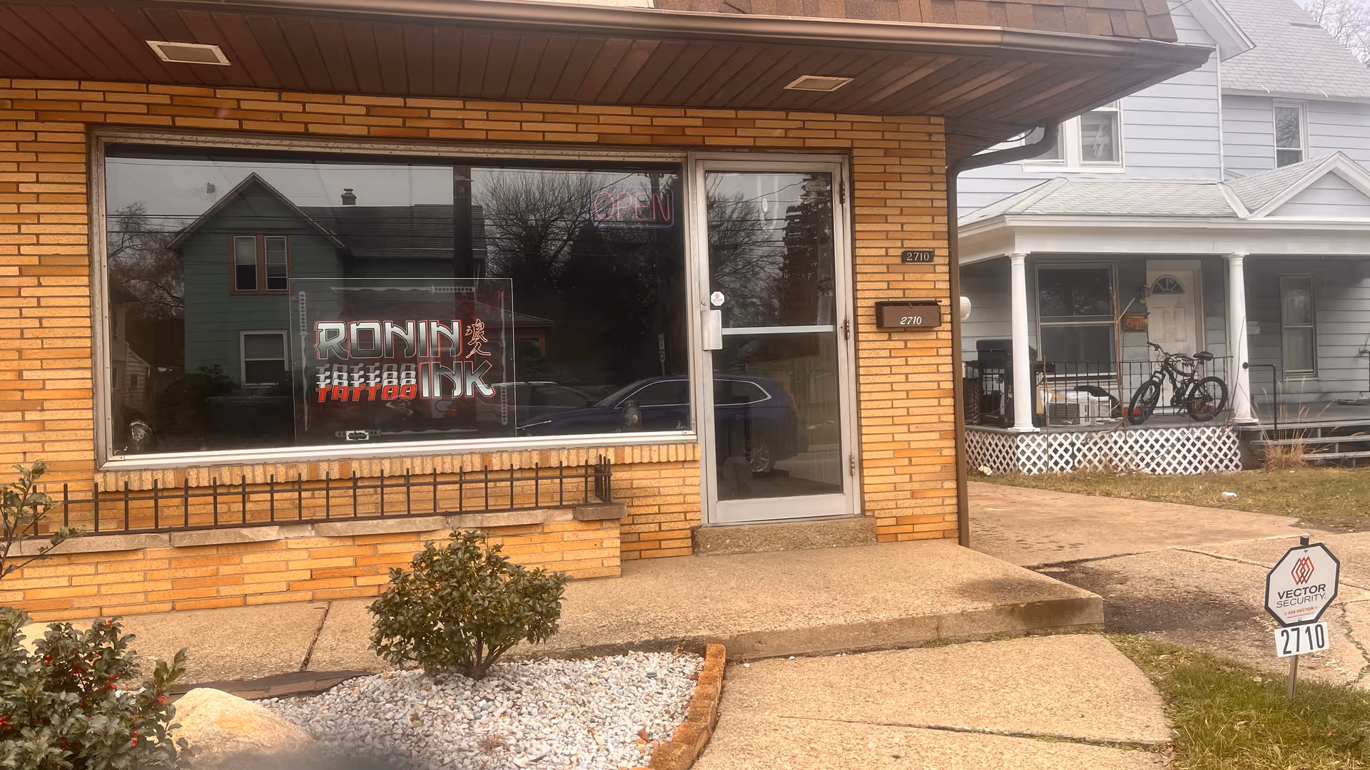Brick storefront with a large window displaying Ronin Ink tattoo sign and a sidewalk.